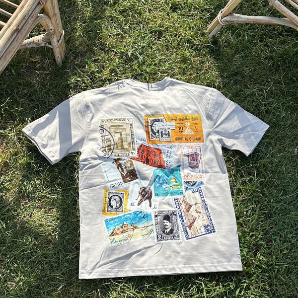 White t-shirt with vintage stamp designs on a grassy surface