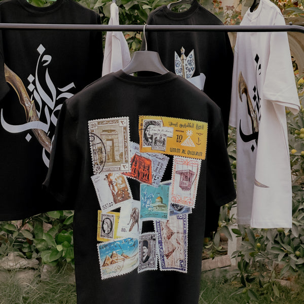Black shirt with vintage stamps design on a rack with other shirts.