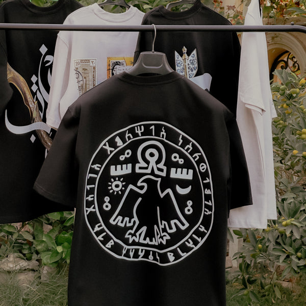 Black shirt with a white symbol design on a rack with other shirts.