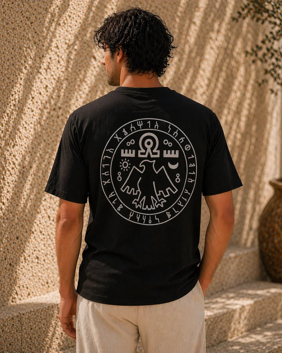 Person wearing a black t-shirt with a white design on the back, standing against a textured wall.
