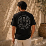 Person wearing a black t-shirt with a white design on the back, standing against a textured wall.