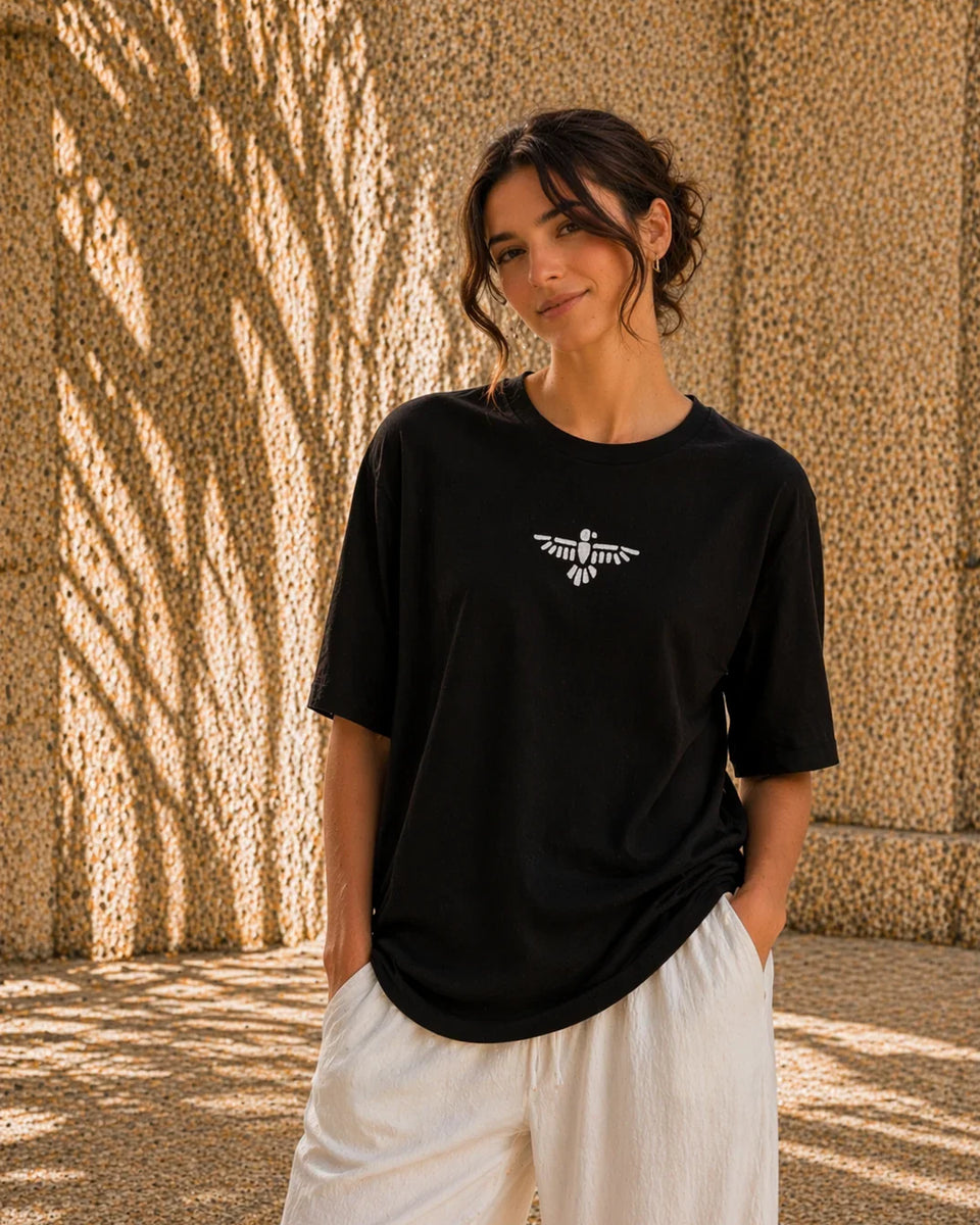Woman wearing a black t-shirt with a white logo against a textured wall.
