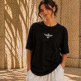 Woman wearing a black t-shirt with a white logo against a textured wall.