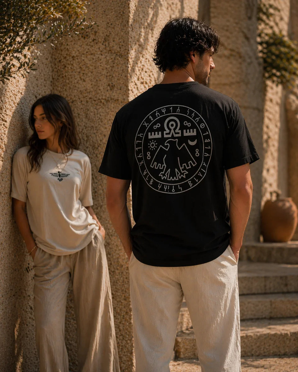 Two people wearing t-shirts with circular designs, standing against a stone wall.