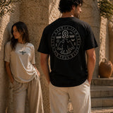 Two people wearing t-shirts with circular designs, standing against a stone wall.