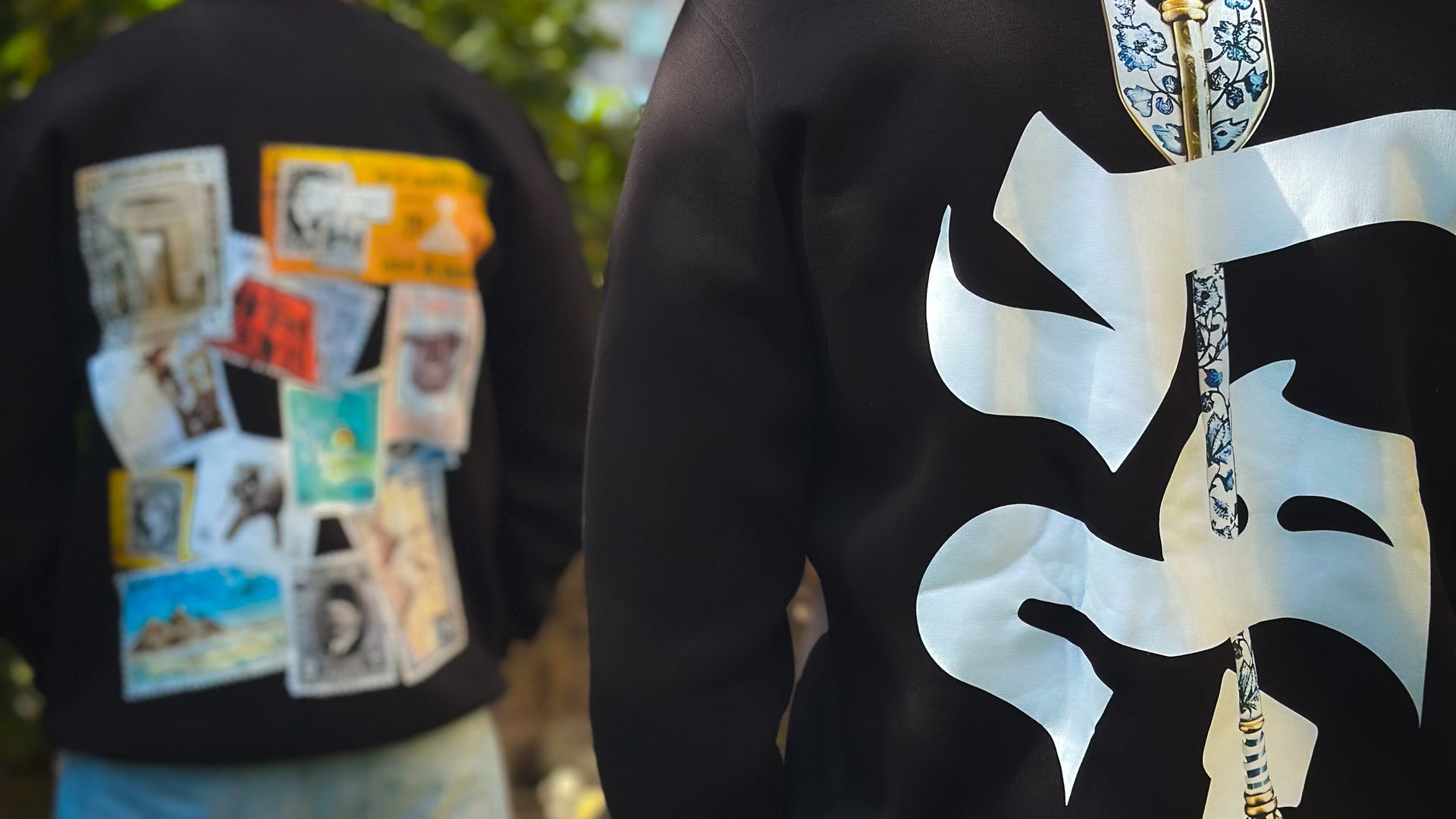  Two people wearing black sweatshirts with unique designs on the back, standing outdoors.