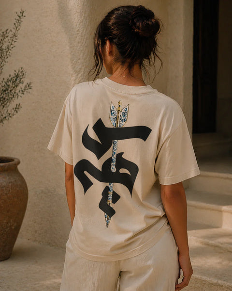 Person wearing a beige t-shirt with a black and white design on the back, standing outdoors.