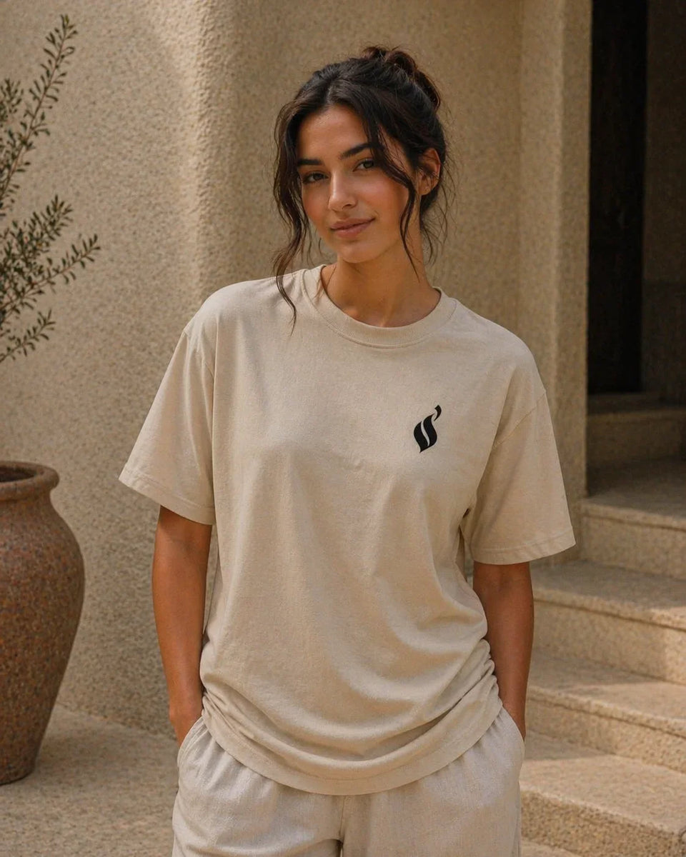 Woman wearing a beige t-shirt with a black logo, standing outdoors.