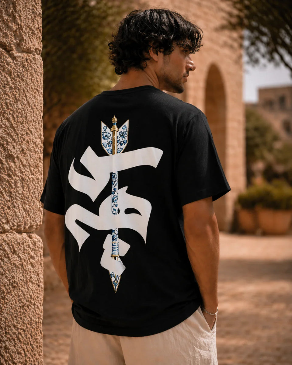 Man wearing a black t-shirt with a white symbol on the back, standing outdoors.