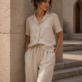 Woman in beige linen outfit standing against a stone wall.