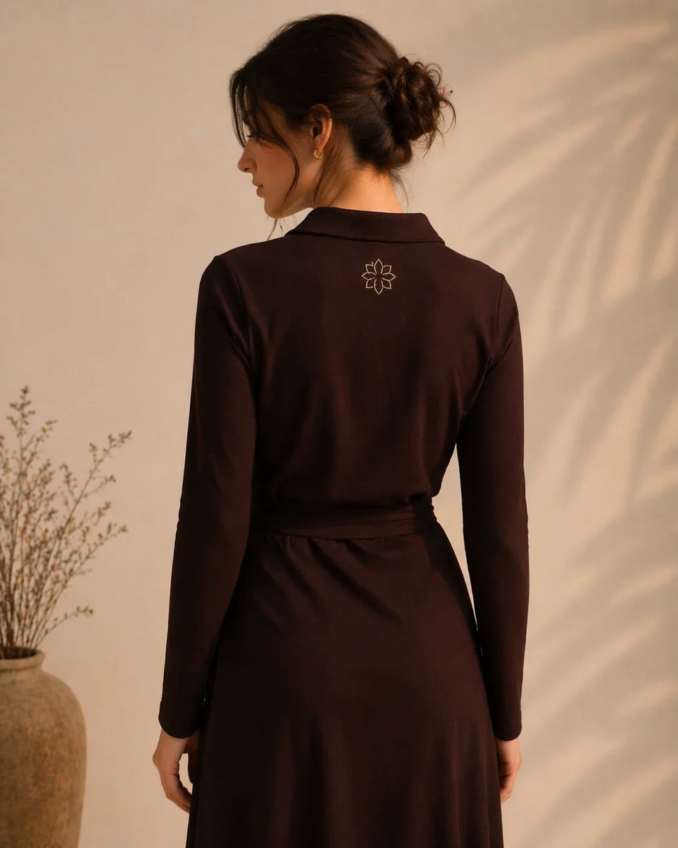 Woman wearing a dark brown dress with a subtle design on the back against a beige wall.