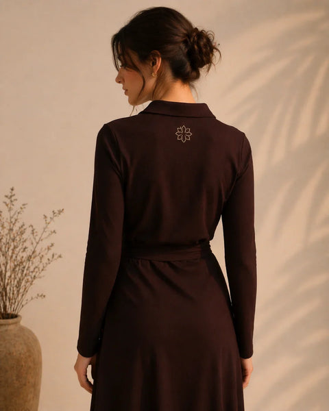 Woman wearing a dark brown dress with a subtle design on the back against a beige wall.