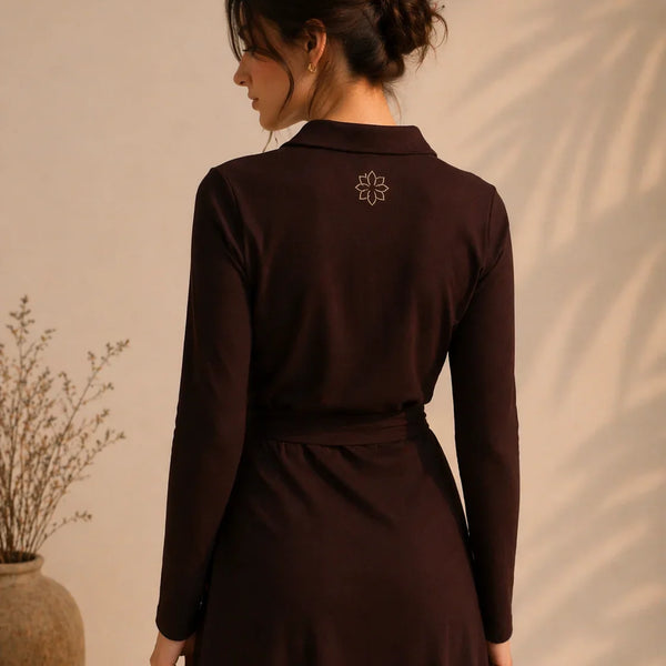 Woman wearing a dark brown dress with a subtle design on the back against a beige wall.