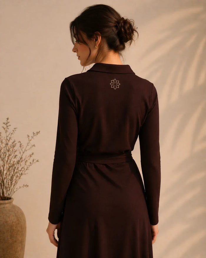 Woman wearing a dark brown dress with a subtle design on the back against a beige wall.