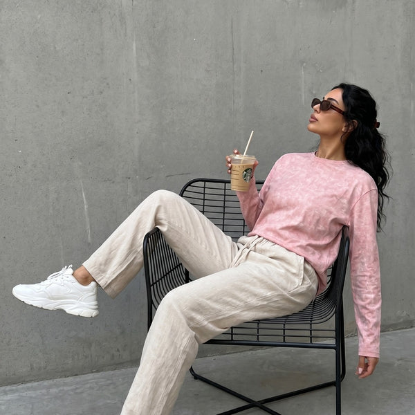 Model in QADIM washed pink long sleeve tee with cream trousers, outdoor editorial look