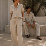Two people wearing light-colored outfits standing in a sunlit outdoor setting.