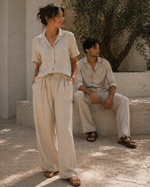 Two people wearing light-colored outfits standing in a sunlit outdoor setting.