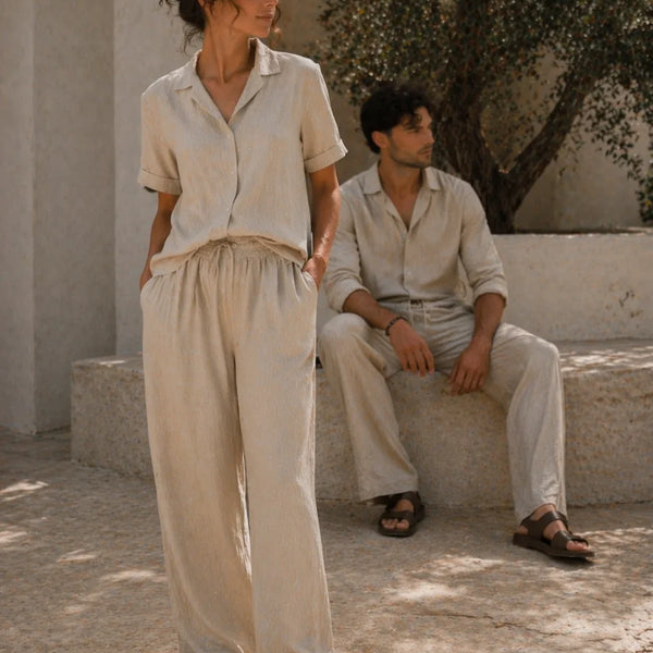 Two people wearing light-colored outfits standing in a sunlit outdoor setting.