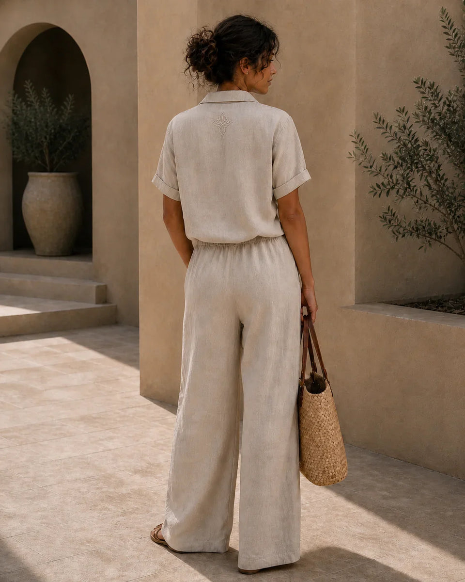 Back view of QADIM sand linen trousers styled on female model in warm courtyard setting
