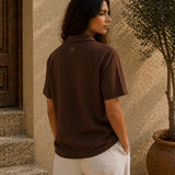 Person wearing a brown polo shirt standing in front of a textured wall and door.