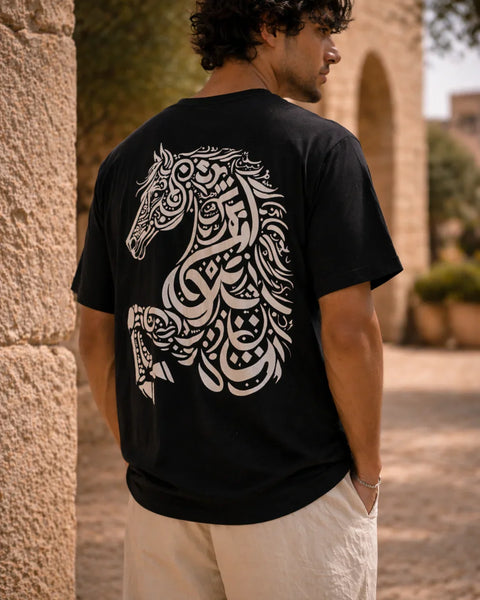 Man wearing a black t-shirt with a white horse design on the back, standing against a stone wall.