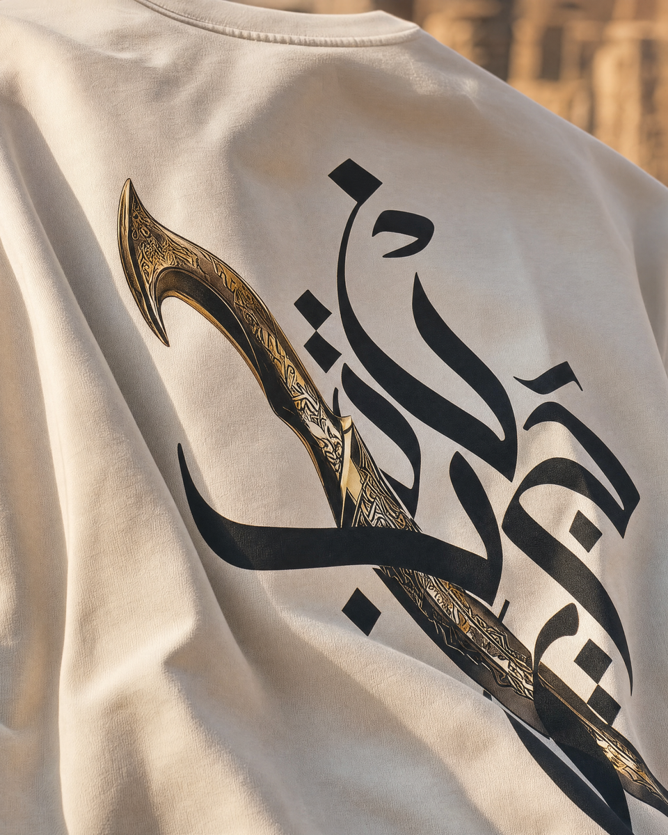 Close-up of Jambiya dagger and Arabic calligraphy graphic print on QADIM Beige t-shirt