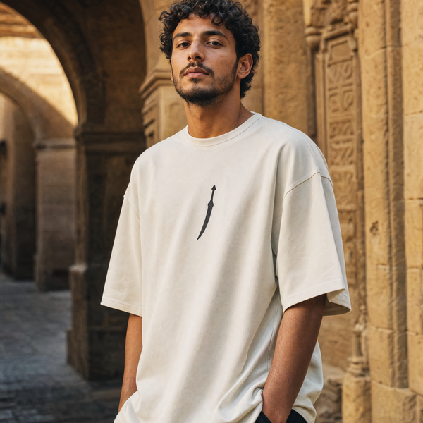 Man wearing QADIM Jambiya Oversize T-Shirt in Beige, front view with small dagger icon on chest