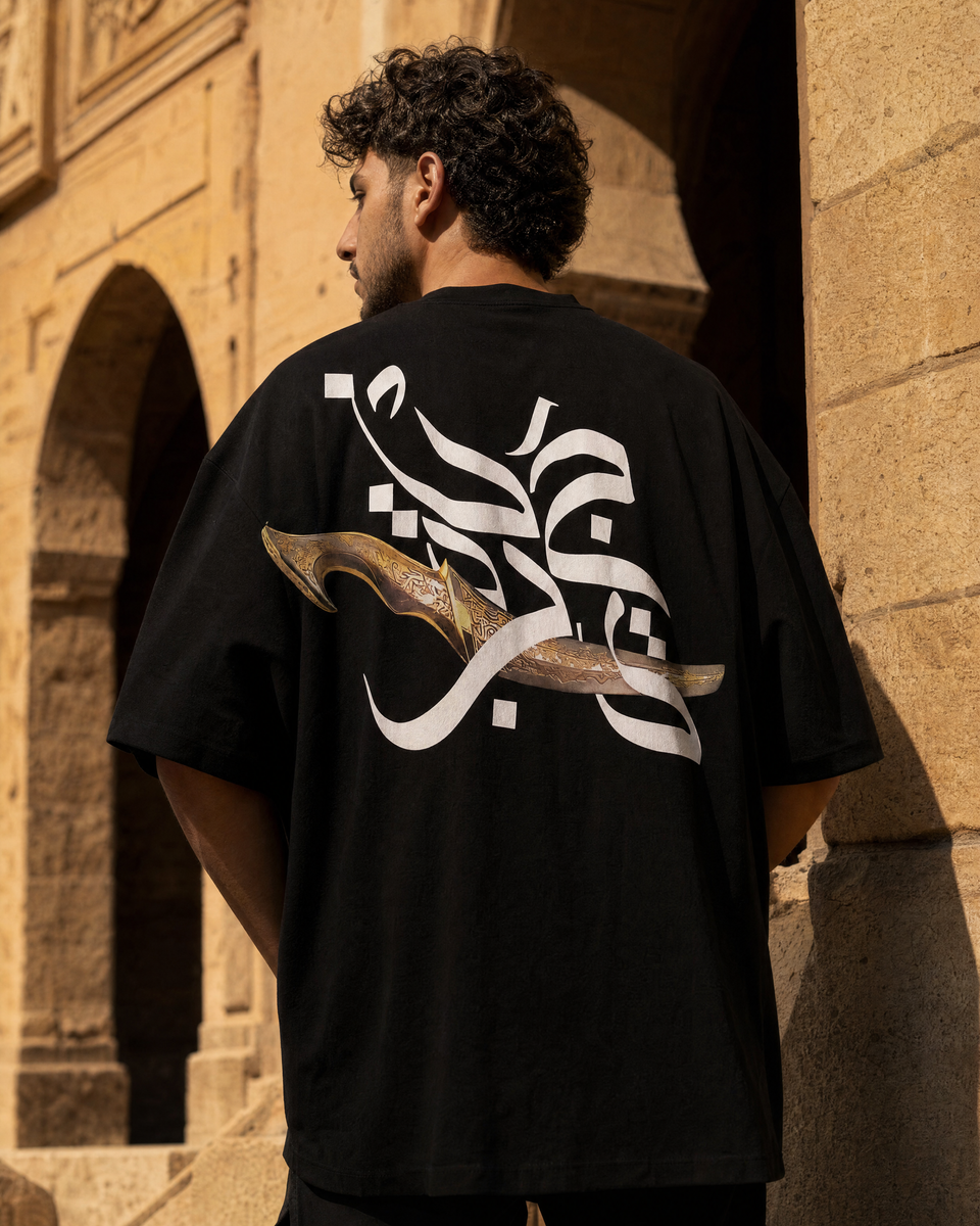 Man wearing QADIM Jambiya Oversize T-Shirt in Black, back view, Cairo heritage archway
