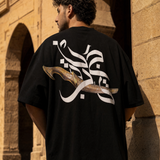 Man wearing QADIM Jambiya Oversize T-Shirt in Black, back view, Cairo heritage archway