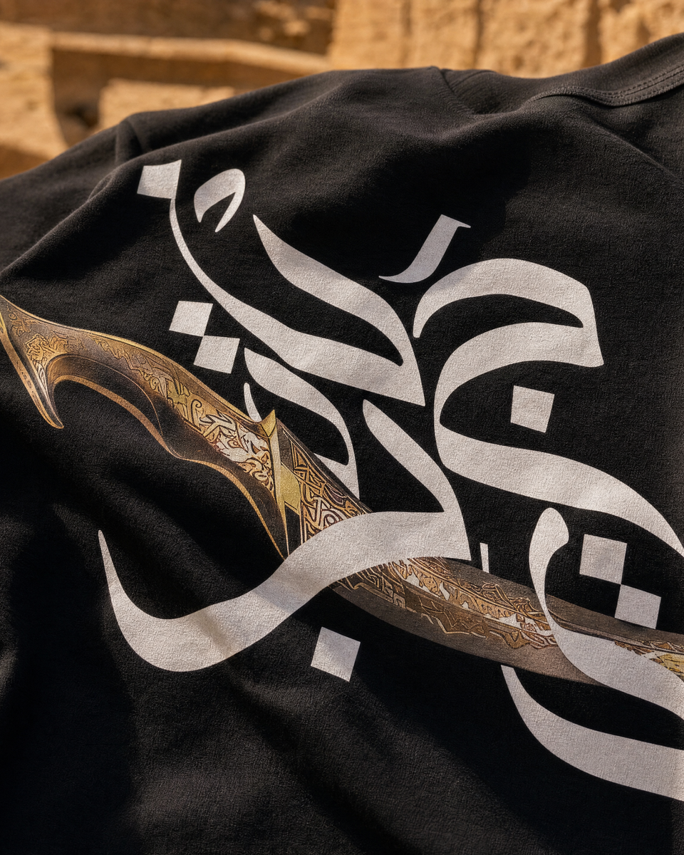 Close-up of Jambiya dagger and Arabic calligraphy graphic print on QADIM Black t-shirt