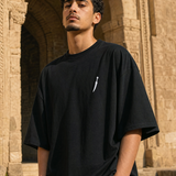 Man wearing QADIM Jambiya Oversize T-Shirt in Black, front view with small white dagger icon on chest