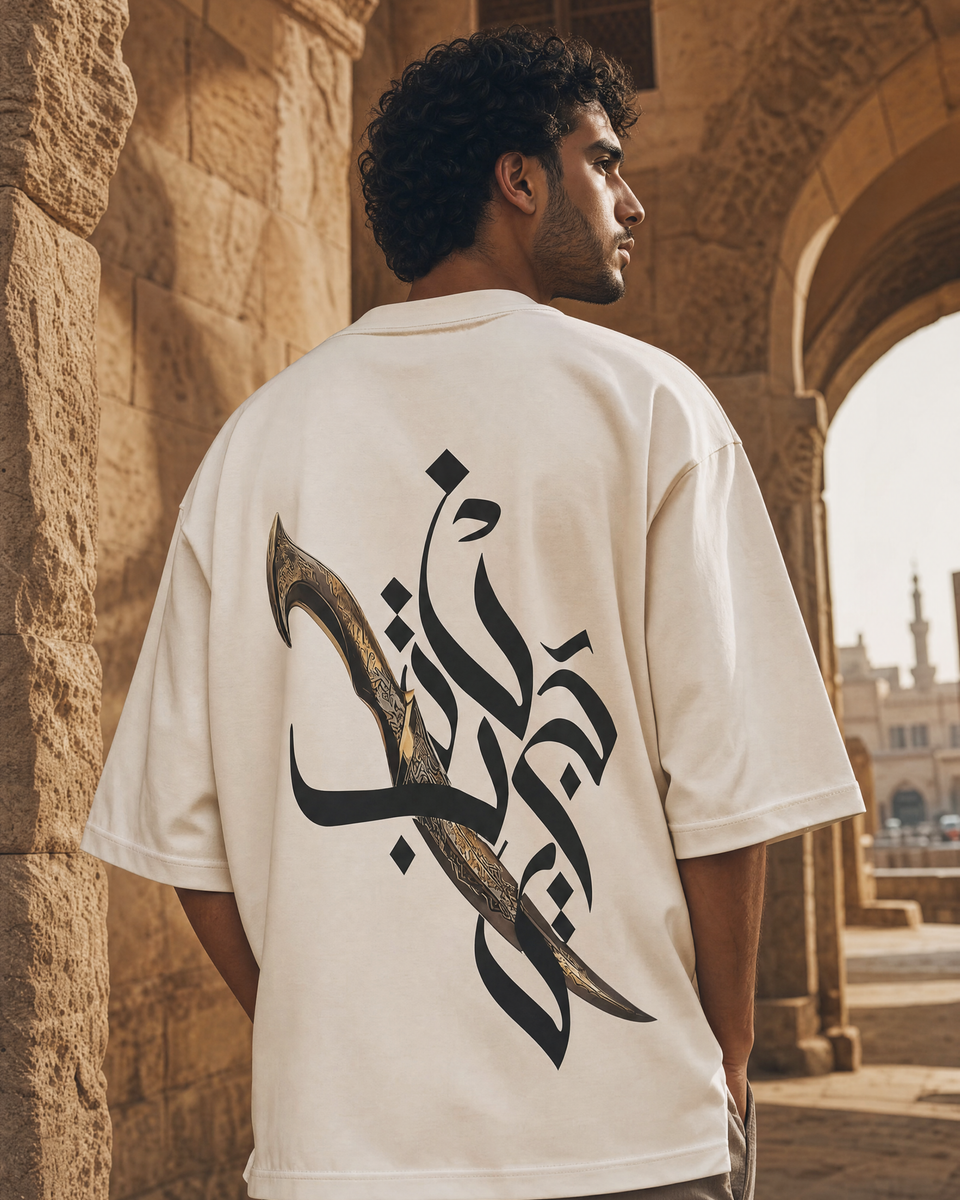Man wearing QADIM Jambiya Oversize T-Shirt in Beige, back view, Cairo heritage archway
