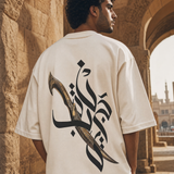 Man wearing QADIM Jambiya Oversize T-Shirt in Beige, back view, Cairo heritage archway