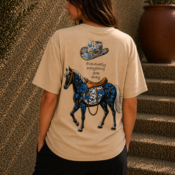 Person wearing a beige t-shirt with a blue horse and cowboy hat design.