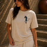 Woman wearing a beige t-shirt with a graphic design, standing against a textured wall.