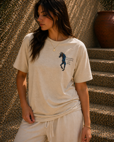 Woman wearing a beige t-shirt with a graphic design, standing against a textured wall.