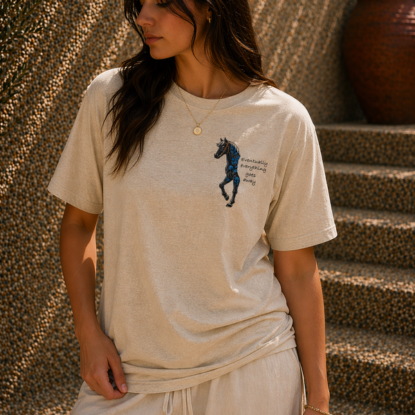 Woman wearing a beige t-shirt with a graphic design, standing against a textured wall.