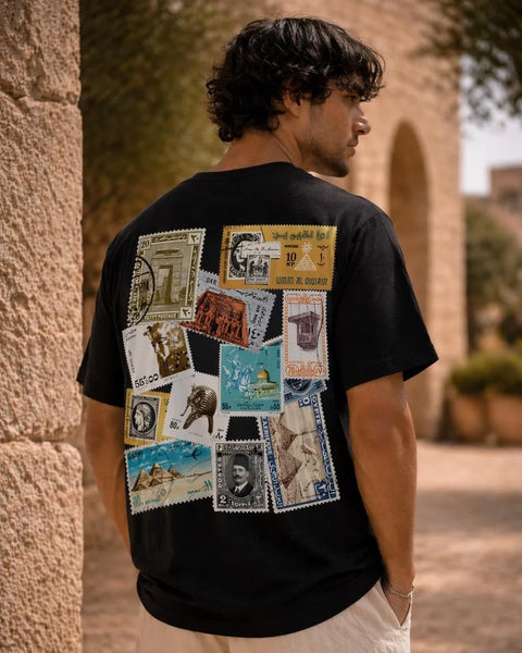Person wearing a black t-shirt with vintage stamp designs on the back, standing outdoors.