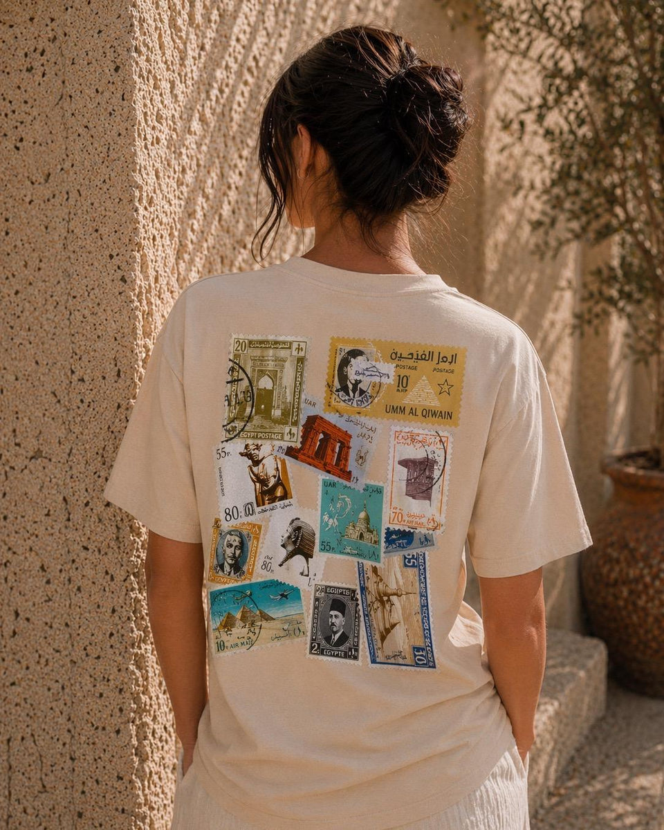 Person wearing a white t-shirt with vintage-style graphic on the back, standing against a textured wall.