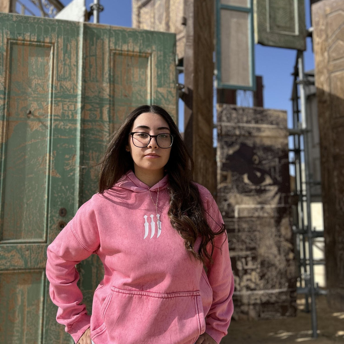 QADIM Jambiya washed hoodie in rose, front, old wooden doors in the desert | هودي جنبية مغسول روز قدام الأبواب القديمة