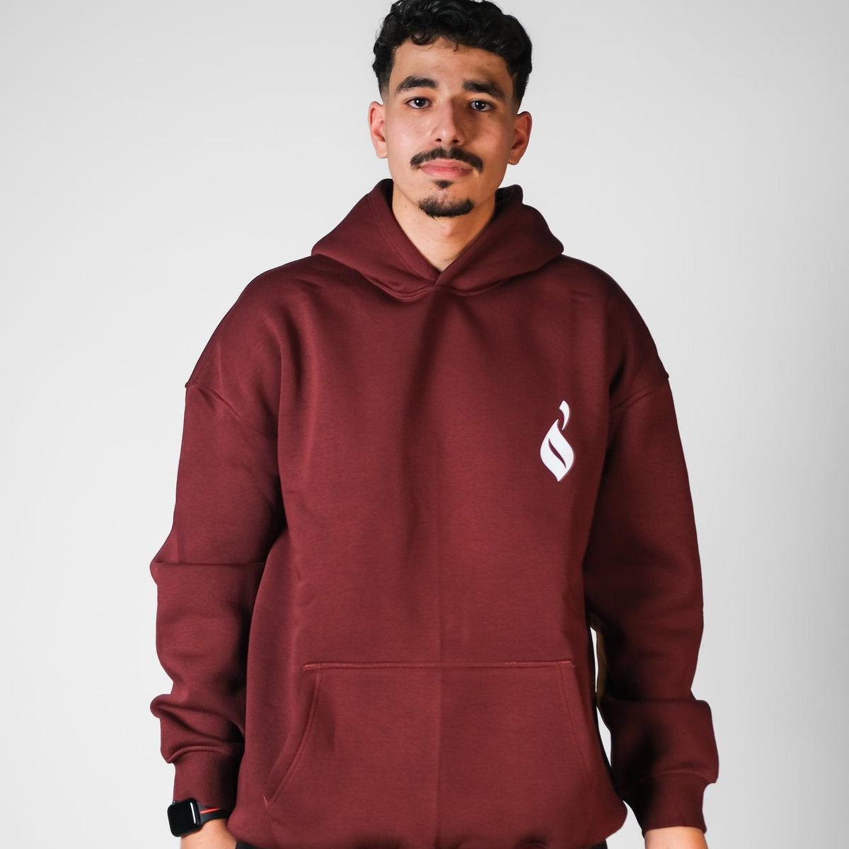 QADIM Sahm relaxed hoodie in burgundy, front emblem, male model | هودي سهم ريلاكس نبيتي من قدّام